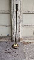 Full view of antique metal floor lamp with tall slender shaft, hexagonal, decorated base, and attached power cord.