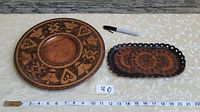 Photo showing the round wooden plate and oval leather plate side by side with measuring tape and black marker for scale.