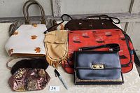 Seven assorted bags in various colors and styles shown together on a table, including handbags, suede bag, and large shoulder bag.