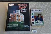 Photo including the unopened 'An Evening of Murder Party Game' box and a Psychogames booklet placed on a table with a floral tablecloth.