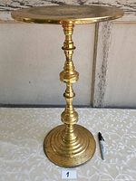 Front view of brass side table showing full height and round brass top with reflective surface.