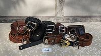 Photo showing all 9 genuine leather belts assorted by color and buckle style on light patterned surface.