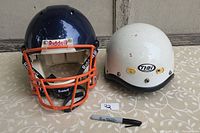Both helmets shown side by side from front angle on patterned surface with marker for scale.