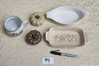 Photo showing assorted kitchen items including porcelain Christmas cup, pumpkin-shaped salt and pepper dispensers, and three small dishes arranged on table with a Sharpie marker for scale.