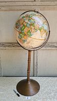 Front view of the globe showing parts of Europe, Asia, and Africa above a bronze metal pedestal base with wooden shaft.