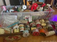 Wide view of assorted rolls of ribbon in a clear plastic bin and spread around it.