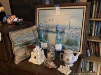 Photo of lot showing oil painting, decorative pillow, two blue glass vases, jar with shells and sand, ceramic teapot, sandcastle figurine and smaller decorative piece