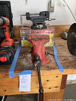 Front view showing 4-inch Central Forge bench vise painted red with black handle and machinist cross slide vise on yellow box behind it.
