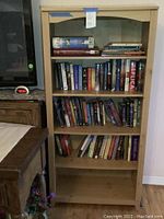 Front view of the wooden 5-shelf bookcase filled with various books to demonstrate shelf size, but contents not included.