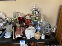 Wide view of the table showing elephant wax warmer, candle sticks, red glass holder, watering can holder, and various candles.
