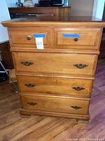 Front view showing four drawers with two small drawers at top with round metal knobs and three larger drawers below with decorative metal handles, overall wood finish.