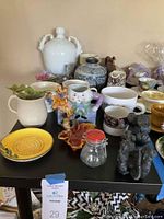 Full view of coffee cups, vases, several decorative figurines, and other small decor items arranged on a table.