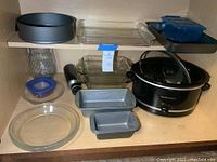 Shelved kitchen items including Hamilton Beach crockpot, glass and metal bakeware, and plastic storage containers.