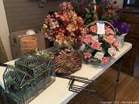Wide view of assorted flower arrangements, baskets, pots, decorative birdcage and ground hangers on display table
