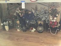 Photo showing multiple faux flower arrangements in ceramic pots and glass vases with varying flower colors including white, purple, and red