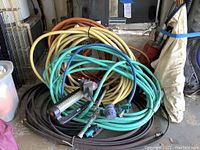 Coiled three garden hoses in green, orange, yellow colors with two black soaker hoses and two sprinklers