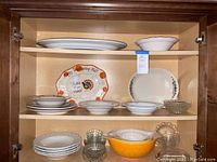 Shelf with various bowls and platters including ceramic Thanksgiving platter, white plates, and clear glass bowls