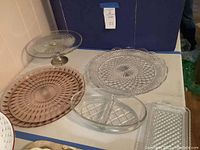 Photo showing the assortment of glass serving pieces on a white surface, including rose-colored platter, clear divided serving dish, and clear crystal platter.