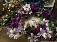 Purple and white floral holiday wreath featuring artificial flowers and decorative butterfly accents