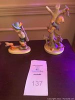 Front view of two Hummel figurines on table with auction tag