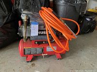 Front-side view of red Husky air compressor with attached orange air hose coiled on top.