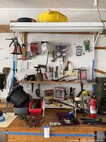 Overview of workbench with various tools, accessories, and hardware items arranged on shelves and table with pegboard wall in background.