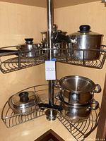 Overview of stainless steel pots arranged on corner metal rack in kitchen cabinet.