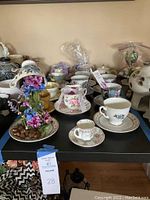 Wide view of table displaying an assortment of teacups, saucers, and the floating teacup floral display with artificial flowers pouring from cup to saucer.