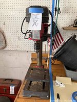 Full front view of the heavy duty drill press placed on a workbench with the adjustable metal table and the drill column visible.