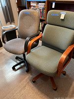 Front view of both upholstered office chairs side by side showing gray chair with plastic arms and legs, green chair with wooden arms and legs and cushioned headrest.