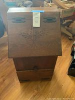 Full front view of wooden bin showing carved wheat/leaf design and two metal handles on top front.
