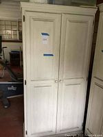 Front view of white wooden pantry cupboard with two closed doors and taped note '204' on one door.