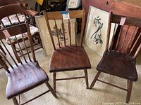 Three different vintage wooden chairs arranged side by side with two framed bird prints behind them.
