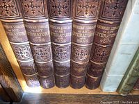 Close-up photo showing five volumes of American Library of Art Literature and Song with ornate brown leather bindings and gold embossed titles.