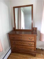 Full view of antique wooden dresser with three drawers and a mirror resting on top, set against a wall with curtains.