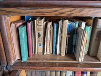 Bookshelf with various Boy Scout handbooks and other books showing wear and age, spines visible with different titles related to scouting and outdoor skills.