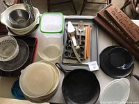 Photo showing two cast iron skillets, plastic containers, metal mixing bowls, glass salad spinner, serving utensils, and wooden signs.