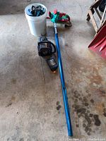 Photo showing all items on floor including bucket with coiled hoses, leaf blower, chainsaw, and an extension cord.