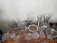 Wide shot of assorted crystal and glassware including bowls, vases, candle holder, and small pitcher on wooden table