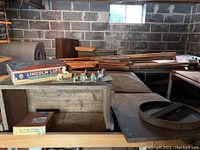 Wide view of basement table with Lincoln Logs box, lead figurines including cowboys and horses, wooden crate, metal train part and stacked wood