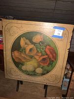 Square wooden fold-down table top with floral artwork and decorative border, showing surface wear.