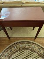 Closed wooden game table with red finish and turned legs shown from the front