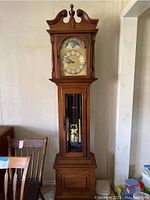 Full view of the tall wooden grandfather clock showing the case, door with glass panel, and crown molding top with finial.