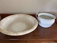 Photo showing large cream-colored ironstone bowl next to white ceramic chamber pot on wooden surface.