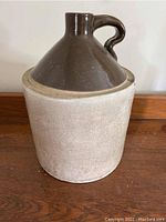 Full view of the large ceramic crock showing beige unglazed body and brown glazed top with handle