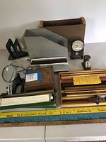 Photo showing various vintage office supplies including slide rule case, bookends, magnifying glass, postage scale, and wooden yardsticks