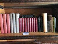Bookshelf showing an assortment of old books including many red and grey hardcover volumes, including Bibles and historical society publications.