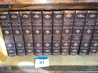 10 volumes of William Shakespeare collected works with brown leather spines and gold embossed titles and designs arranged on a shelf.