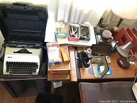 Portable Royal manual typewriter in black hard carrying case among various office supplies on wooden desk.
