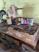 Photo of small cardboard box labeled Southern Valley containing various hand tools and hardware on wooden workbench, with Electro Airless Paint Gun box visible behind.